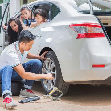 a man fixing car tyer and his family is sitting in the car