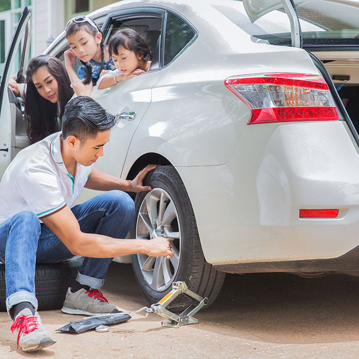 a man fixing car tyer and his family is sitting in the car