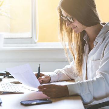 a women with specs sitting holding a pen and a paper 